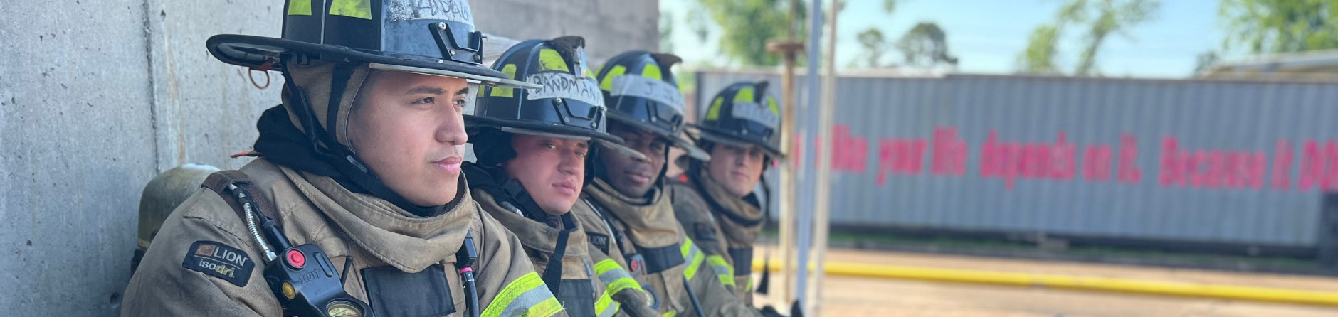 four firefighters sitting along wall with gear